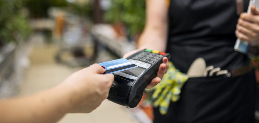 Person hält Karte an das Kartenzahlungsgerät, um kontaktlos zu bezahlen