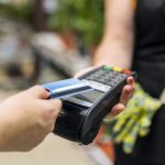 Person hält Karte an das Kartenzahlungsgerät, um kontaktlos zu bezahlen